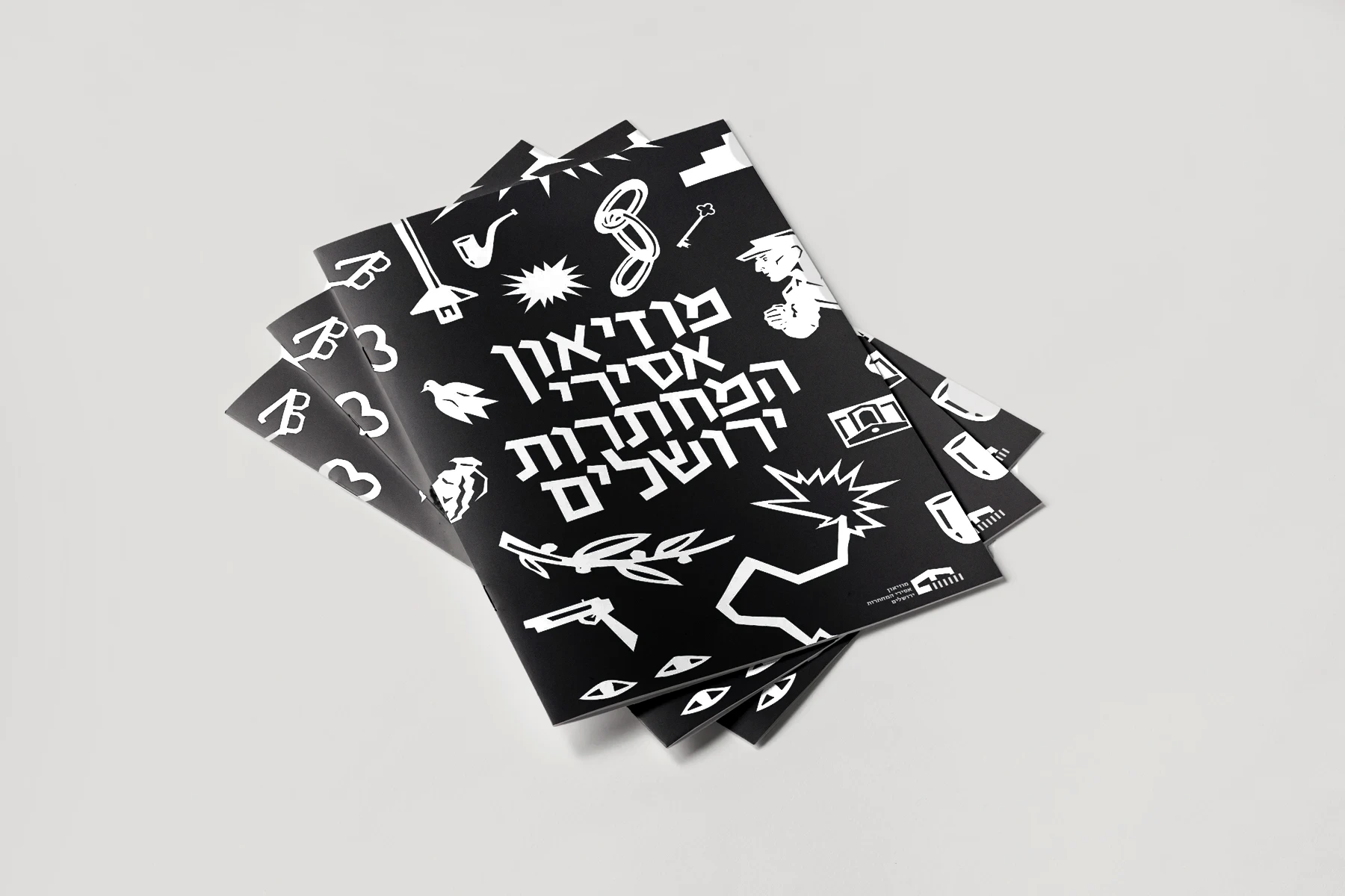 Stack of black museum booklets with white icons and the Hebrew museum name on the cover